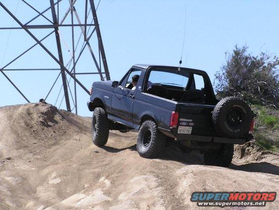 Black 1990 Ford Bronco climbing a dirt hill with a spare tire on the back
