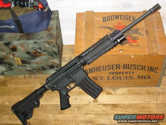 Black assault rifle with a magazine, resting on a wooden surface near a Budweiser crate and a locked chest