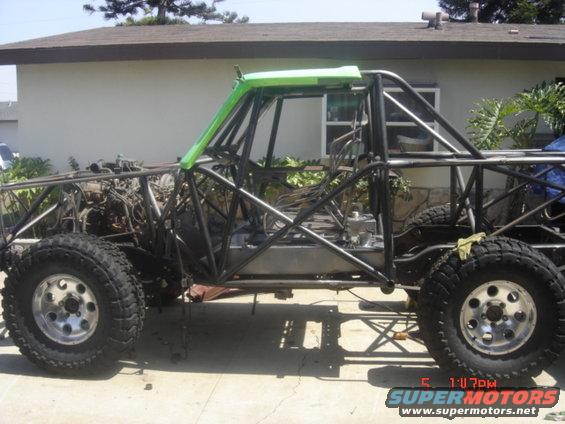 Custom off-road vehicle frame with roll cage, engine, and large tires, in a driveway