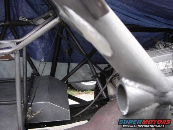 Roll cage tubing and metal box under blue tarp, with a tire visible in the background