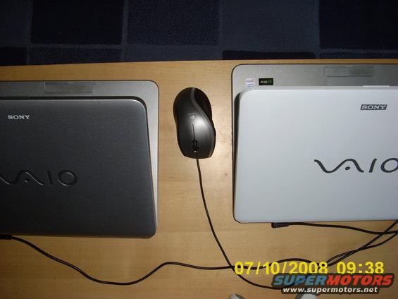 Two Sony VAIO laptops, one dark gray and one white, with a computer mouse between them on a wooden surface