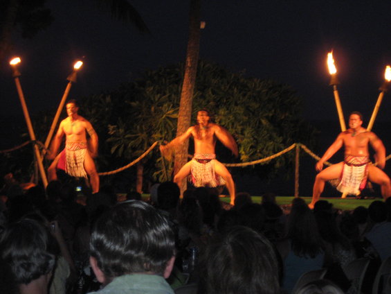 Three men perform a traditional dance with torches at night in front of an audience