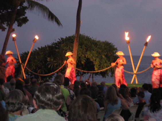 People watching hula dancers perform by torches near the ocean at dusk