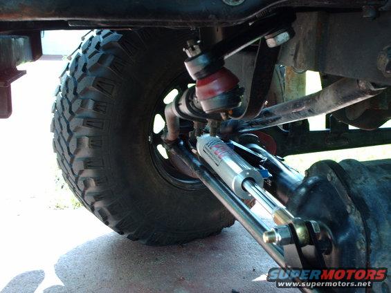 Close-up of a vehicle's front suspension with a large tire and a hydraulic steering stabilizer