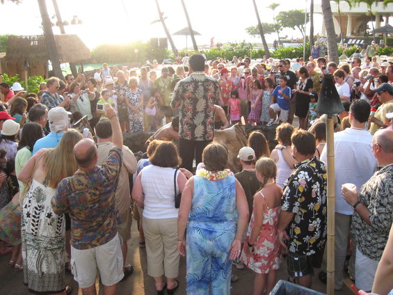 Crowd gathered outdoors for an event, with palm trees and a building in the background