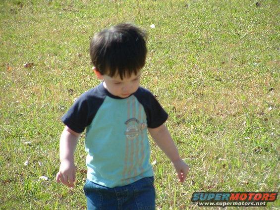 Young boy in a blue and black shirt and jeans walks in a grassy field