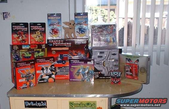 Collection of Transformers and Robotech toys on a shelf, including boxed figures and a small dog toy