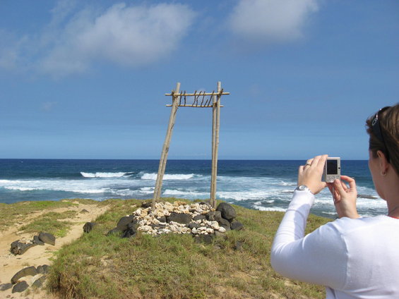 Woman with digital camera photographs wooden archway and rocks on grassy cliff overlooking ocean waves