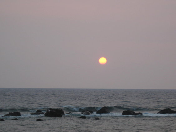 Sunset over the ocean with waves breaking on rocks in the foreground