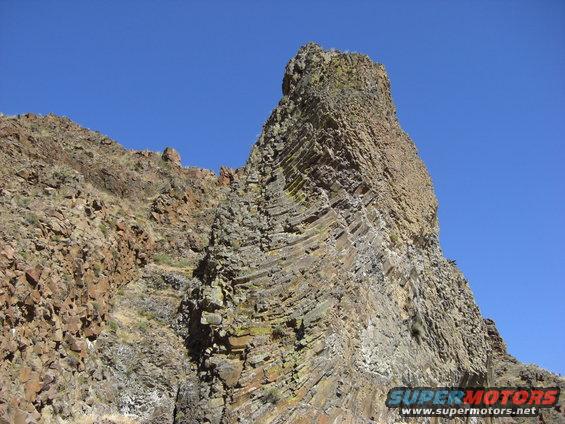 Rocky cliff face with layered geological formations under a clear blue sky