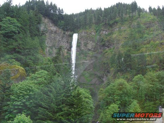 Tall waterfall cascading down a rocky cliff face surrounded by dense green forest