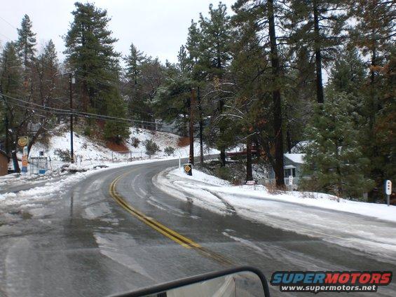 Curving road with snow on the sides and trees on a cloudy day