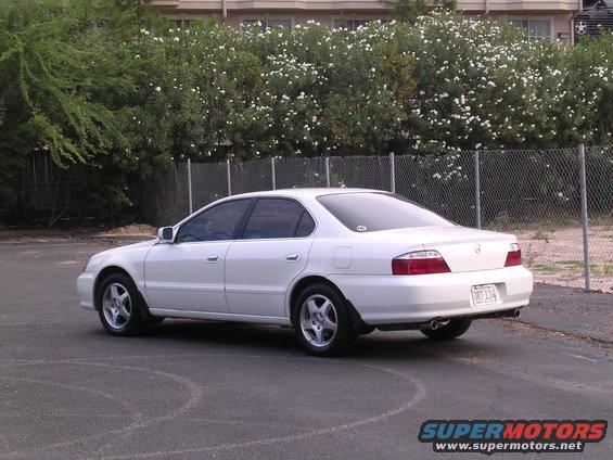 White 2003 Acura TL sedan from rear-right, parked on asphalt with a fence and bushes behind
