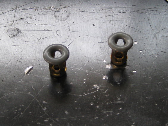 Two brass and gray plastic grommets on a scratched metal surface