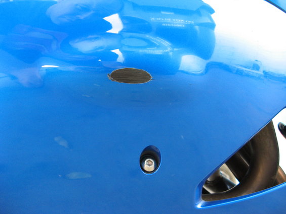Close-up of blue motorcycle fairing showing a scraped area and a bolt hole
