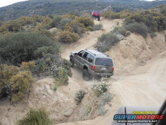 Gray Jeep Grand Cherokee descending a dusty trail with a red SUV behind it