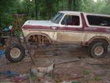 White and maroon Ford Bronco with rust and missing front fender, viewed from the side