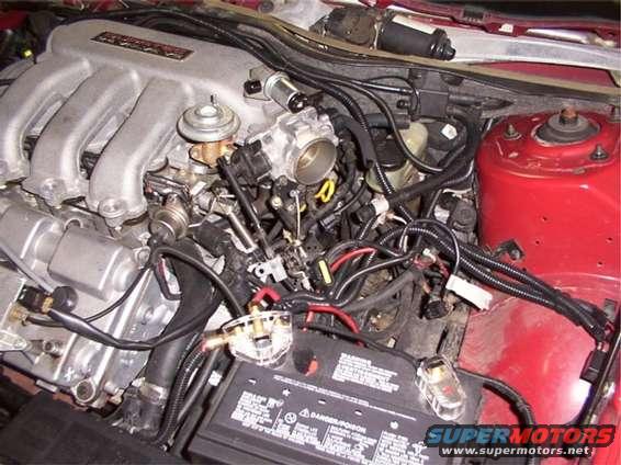 Engine manifold and throttle body with wiring and battery in a red engine bay