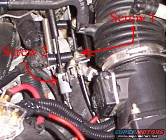 Close-up of engine hoses and intake components with red arrows pointing to screws
