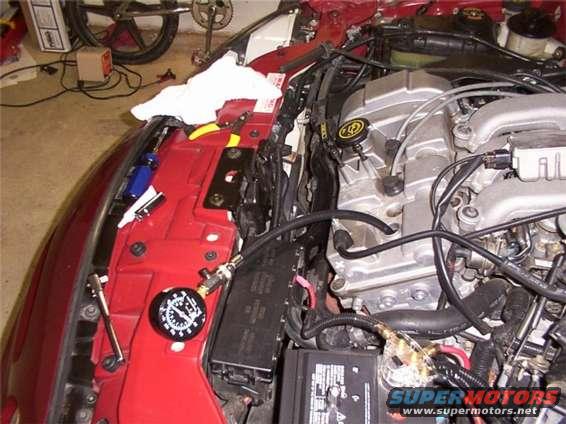 engine bay with pressure gauge attached to fuel rail, showing Ford logo on intake manifold