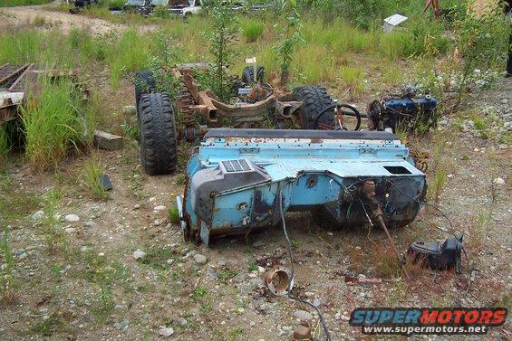 Disassembled light blue vehicle chassis with engine and large tires in a junkyard