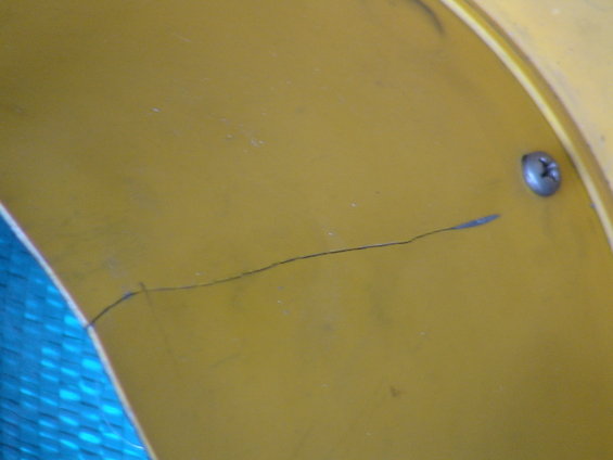 Yellow painted surface with a thin crack running across it and a silver screw on the right side