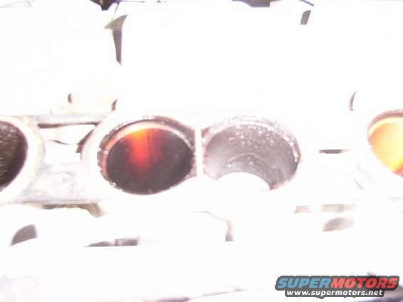Close-up of engine intake ports, one with dark residue, the other with water droplets. Supermotors logo visible at bottom right