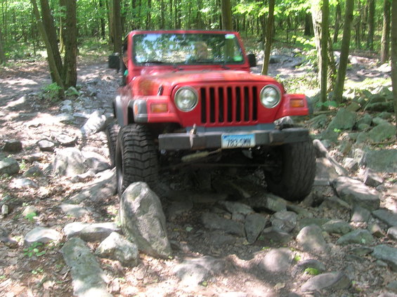 Red Jeep Wrangler navigating a rocky forest trail