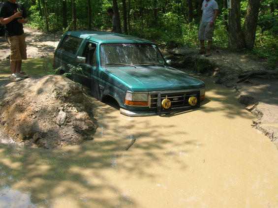 Green Ford Bronco stuck in a mud pit with KC lights on the front