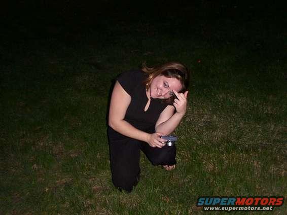 Woman kneeling in grass, holding a camera and giving the middle finger