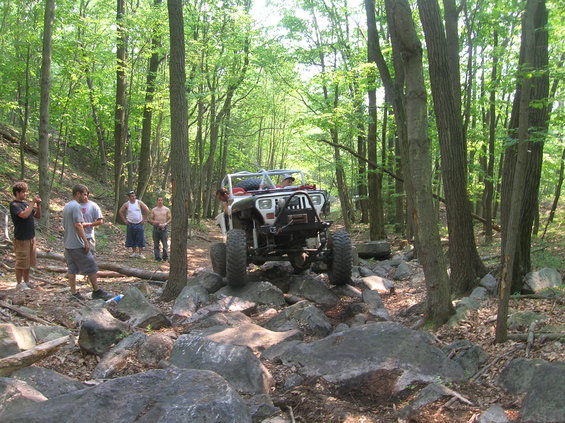 Jeep driving over rocks in a forest with people watching
