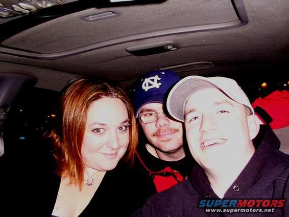 Three people smiling inside a car, with a sunroof visible