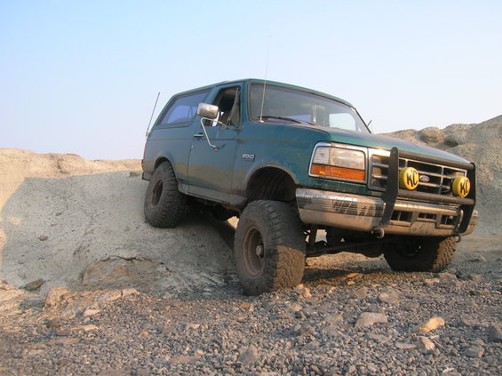 Green 1996 Ford Bronco with off-road tires and brush guard climbing a dirt mound