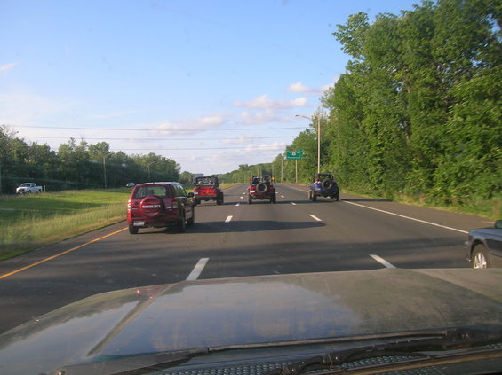 Several Jeeps and a red Suzuki SUV driving on a highway