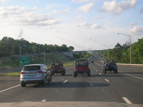 Several Jeeps driving on a highway, with a silver SUV in the foreground. Exit 43 sign visible