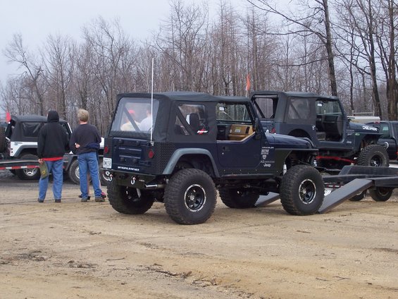 Dark blue Jeep Wrangler with lifted suspension and large tires, parked next to another Jeep on a trailer