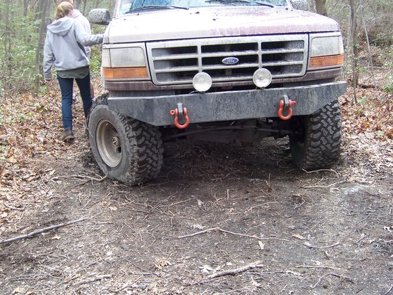 Front view of a 1996 Ford Bronco with an aftermarket bumper and off-road tires. A person stands to the left