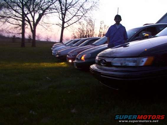 Several sedans parked in a row at dusk, with a person standing next to the closest car