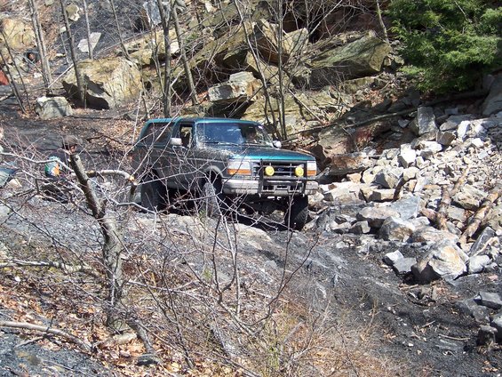 Green Ford Bronco off-roading on a rocky, wooded trail
