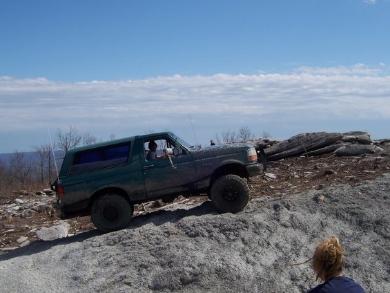 1996 Ford Bronco climbing a rocky incline under a blue sky with scattered clouds