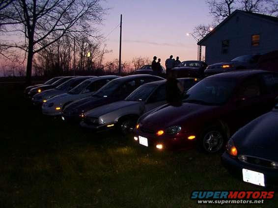 Several cars parked in a line at dusk with a house in the background