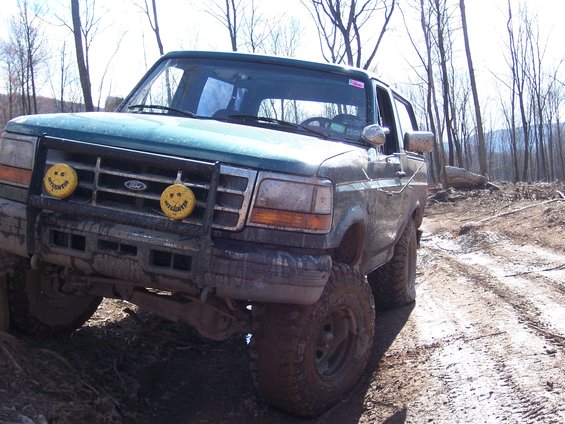 Green 1996 Ford Bronco with brush guard and yellow fog lights on a muddy trail