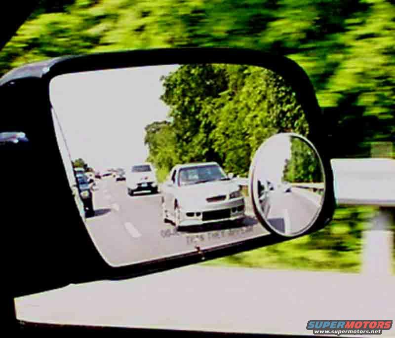 Cars on a highway reflected in a side mirror, with trees blurred in the background