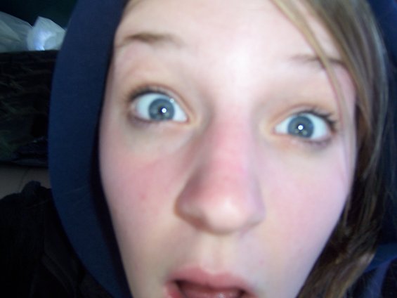 Close-up of a young person's face with wide eyes and an open mouth, wearing a dark hoodie