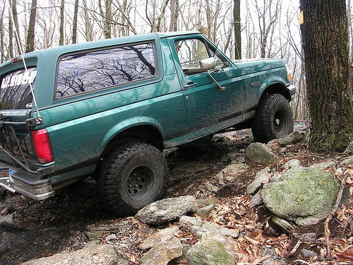 Green 1996 Ford Bronco on a rocky trail, rear-left quarter view, tires on rocks