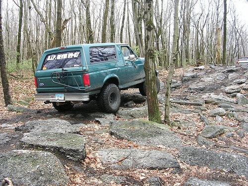 Green 1996 Ford Bronco on a rocky off-road trail, spare tire mounted on rear door