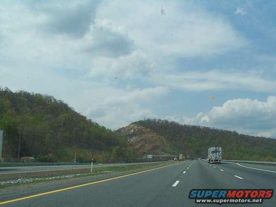 Driving on a highway with trucks ahead and hills on the side