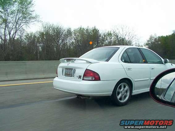 white sedan with spoiler driving on highway, seen from the side rear
