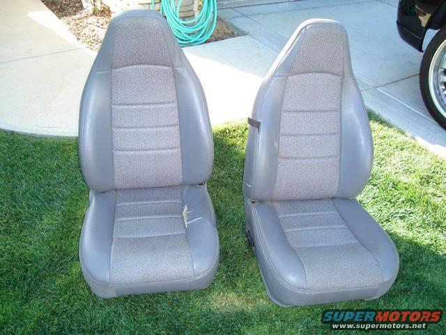 Two gray fabric and leather car seats on grass, one with a tear