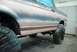 1996 Ford Bronco - A vehicle's side is shown, covered in primer and masking tape, with tires protected during the painting process.